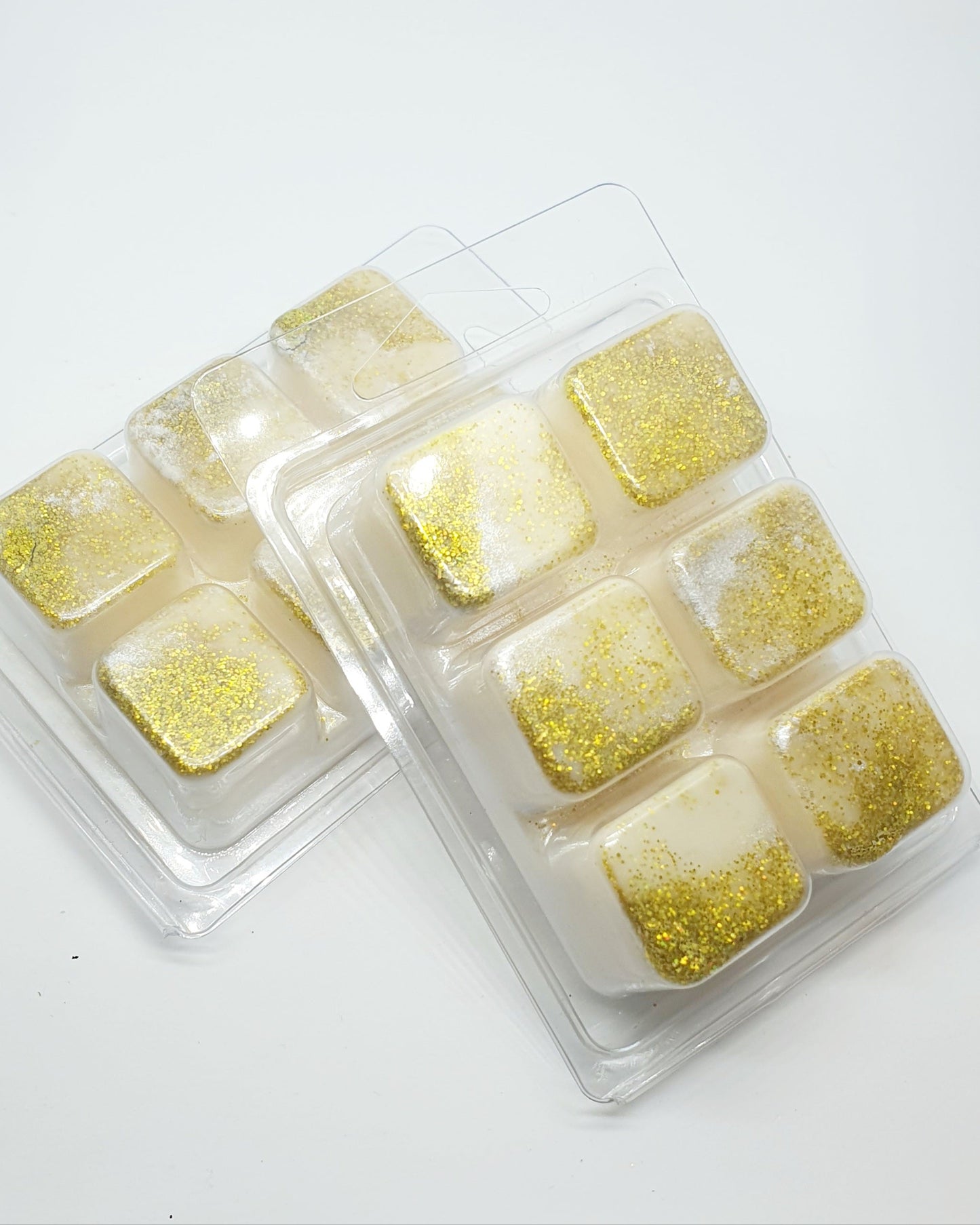 Two clear containers filled with gold and white marbled wax cubes on a white background