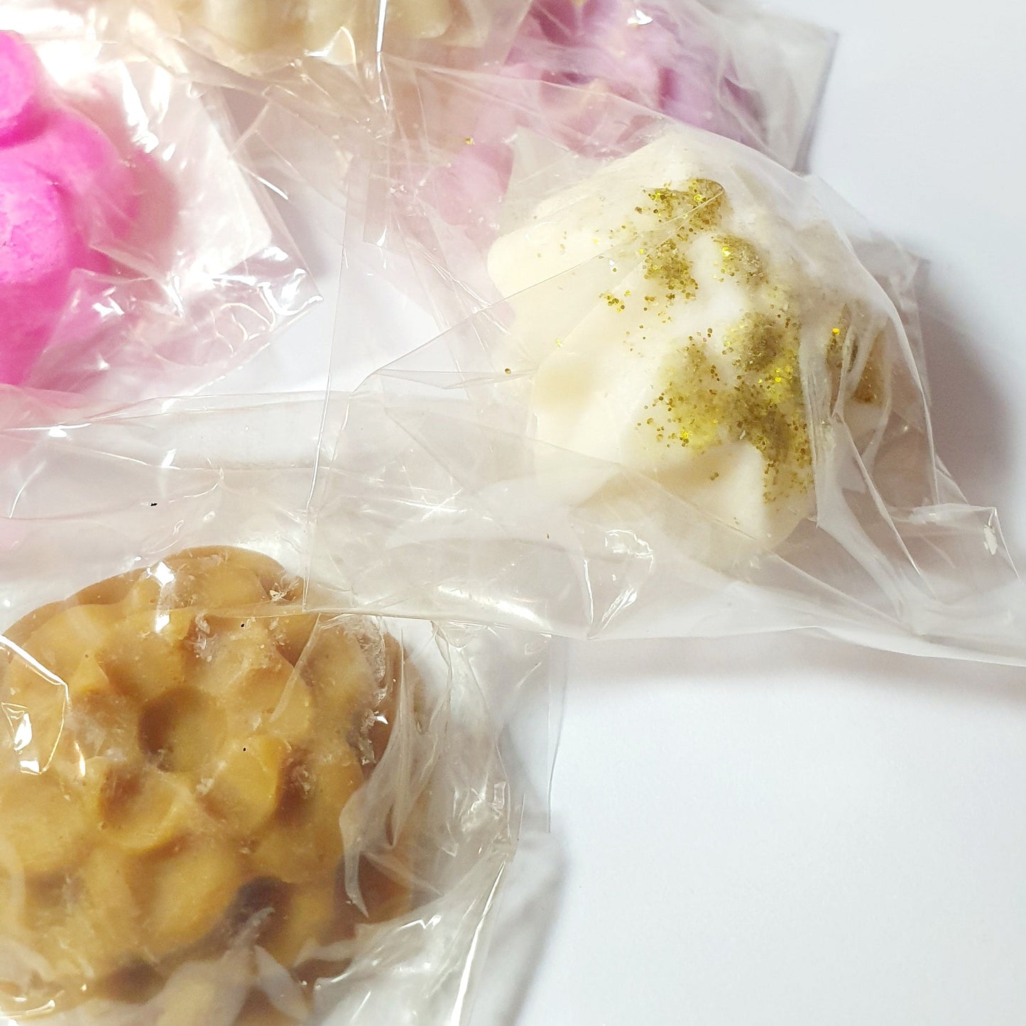Assorted colorful soy wax melt tarts in clear plastic bags on a white background