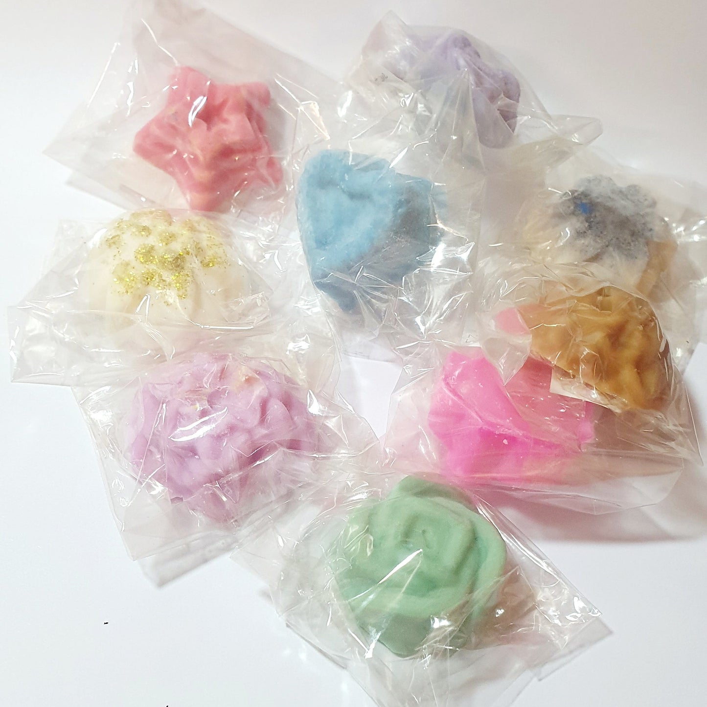Assorted colorful soy wax melt tarts in clear plastic bags on a white background