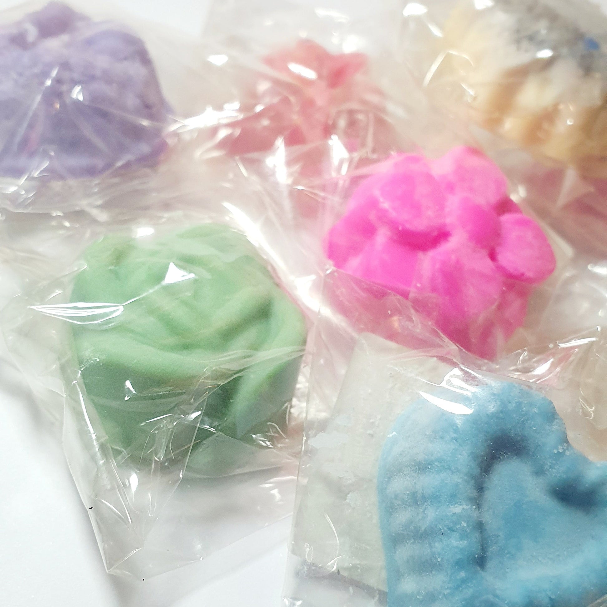 Assorted colorful soy wax melt tarts in clear plastic bags on a white background