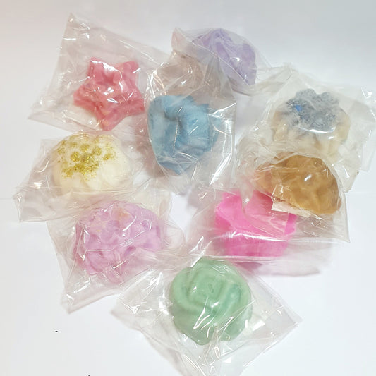Assorted colorful soy wax melt tarts in clear plastic bags on a white background