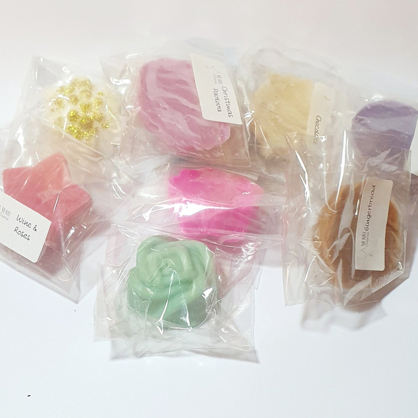 Assorted colorful soy wax melt tarts in clear plastic bags on a white background